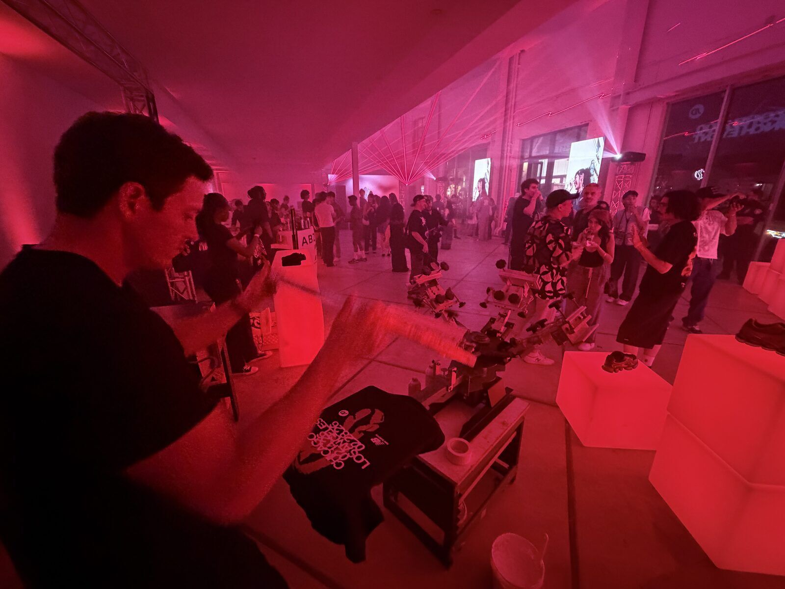 A printer flooding ink across a screen on the press while a packed crowd looks on under red lasers