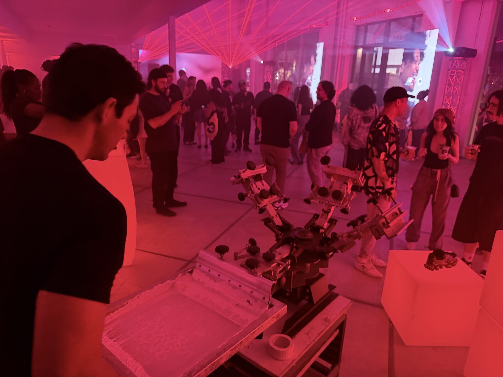 After-dark event crowd gathered around a live press station under pink light at an LA brand activation